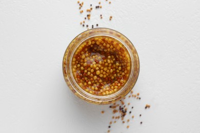 Fresh whole grain mustard in bowl and dry seeds on white table, flat lay