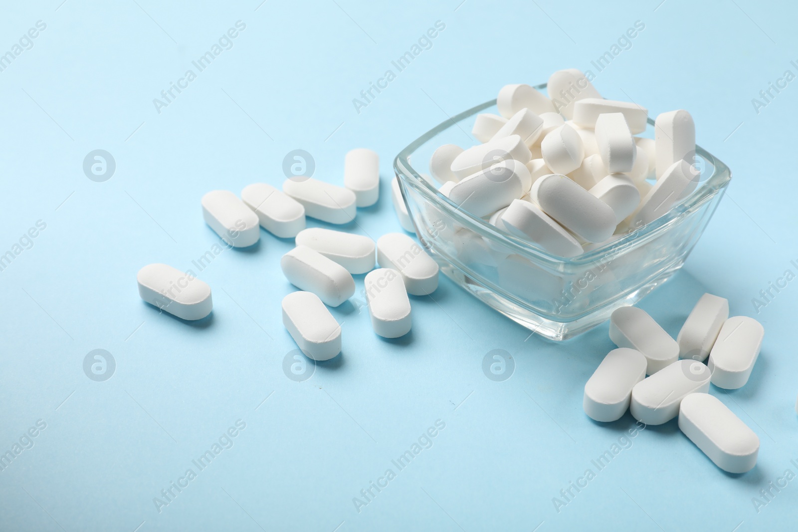 Photo of Vitamin capsules in bowl on light blue background, space for text