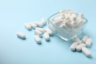 Vitamin capsules in bowl on light blue background, space for text