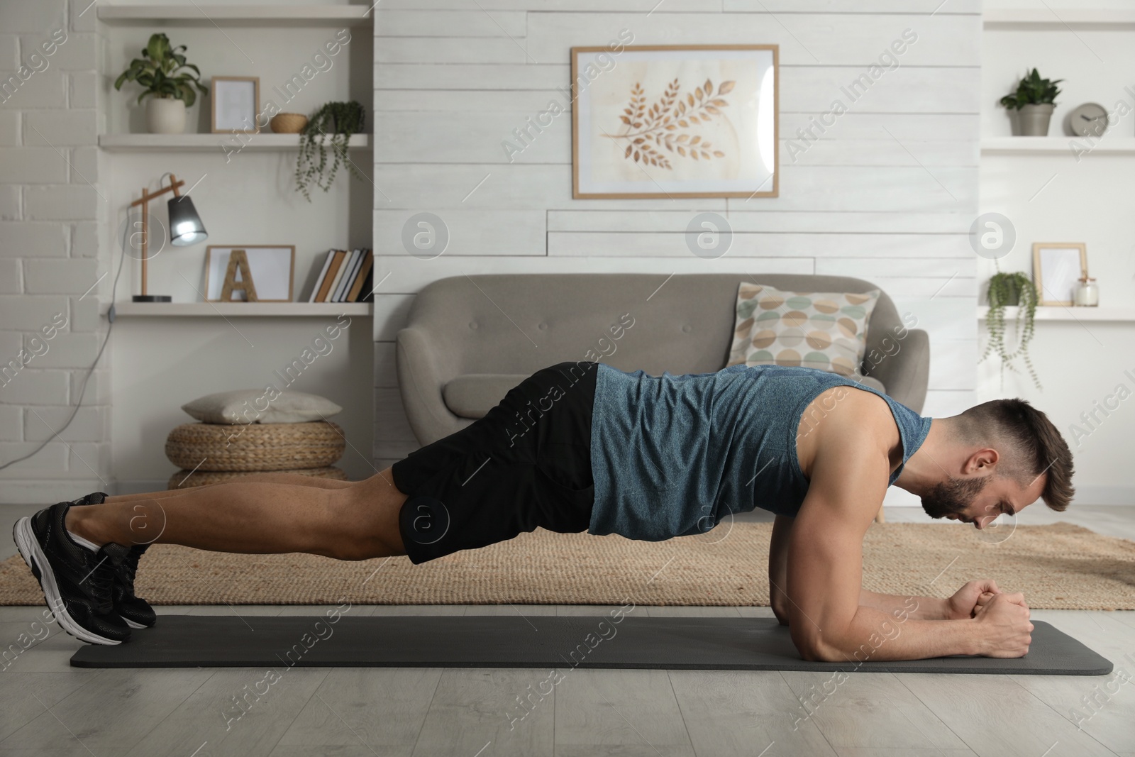 Photo of Handsome man doing plank exercise on yoga mat at home