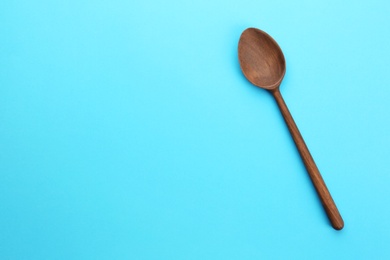 Clean empty wooden spoon on blue background, top view. Space for text