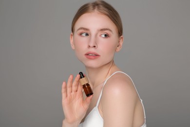 Photo of Beautiful young woman with bottle of essential oil on light grey background