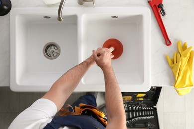 Photo of Plumber using plunger to unclog sink drain, top view