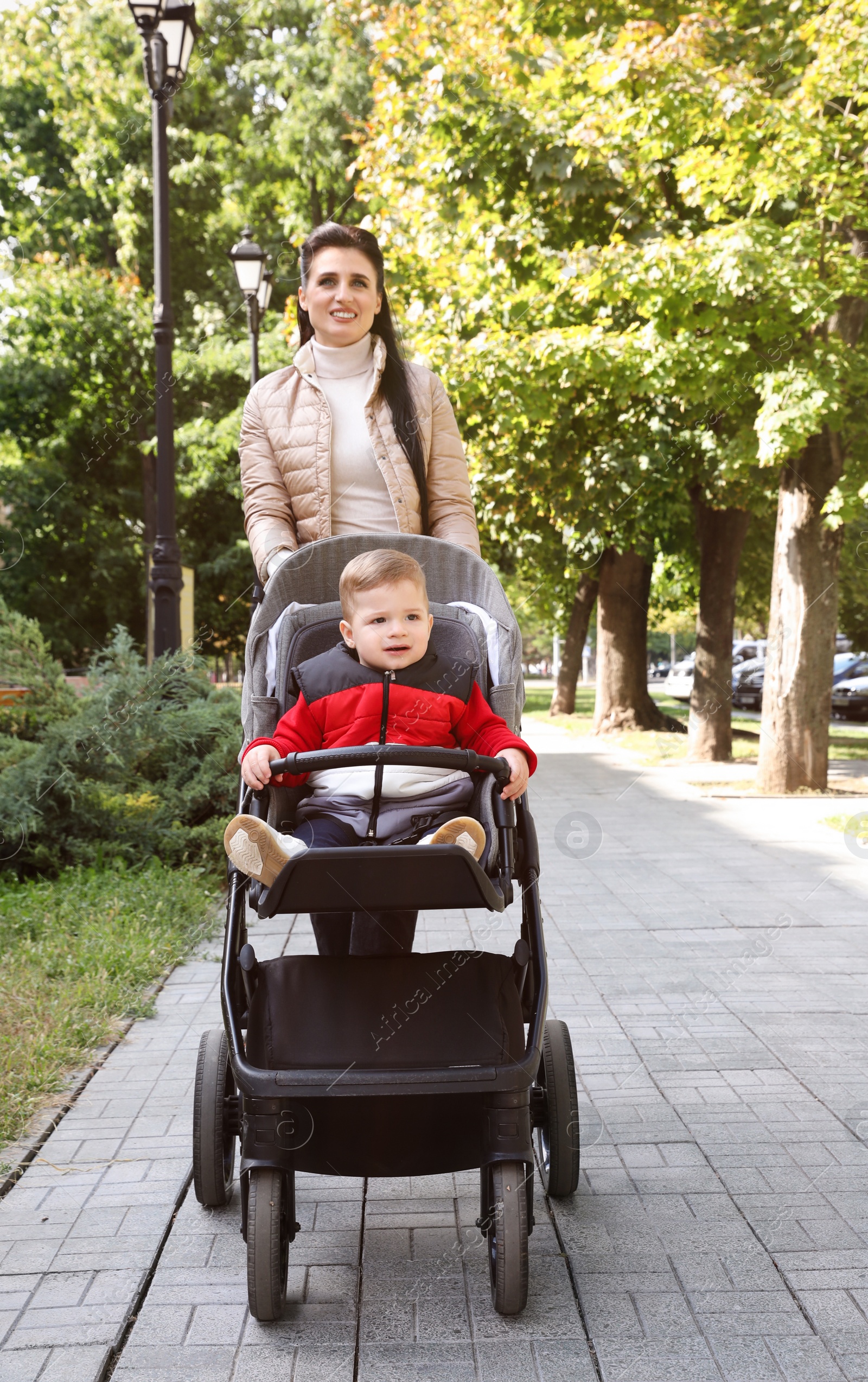 Photo of Happy mother walking with her son in stroller outdoors