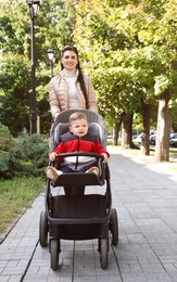 Happy mother walking with her son in stroller outdoors