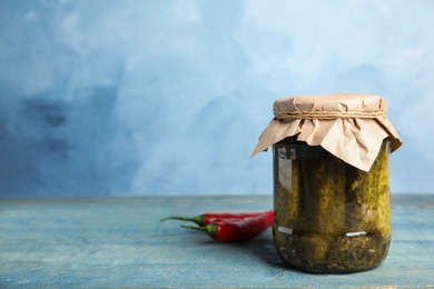 Photo of Jar with pickled cucumbers on wooden table against blue background, space for text