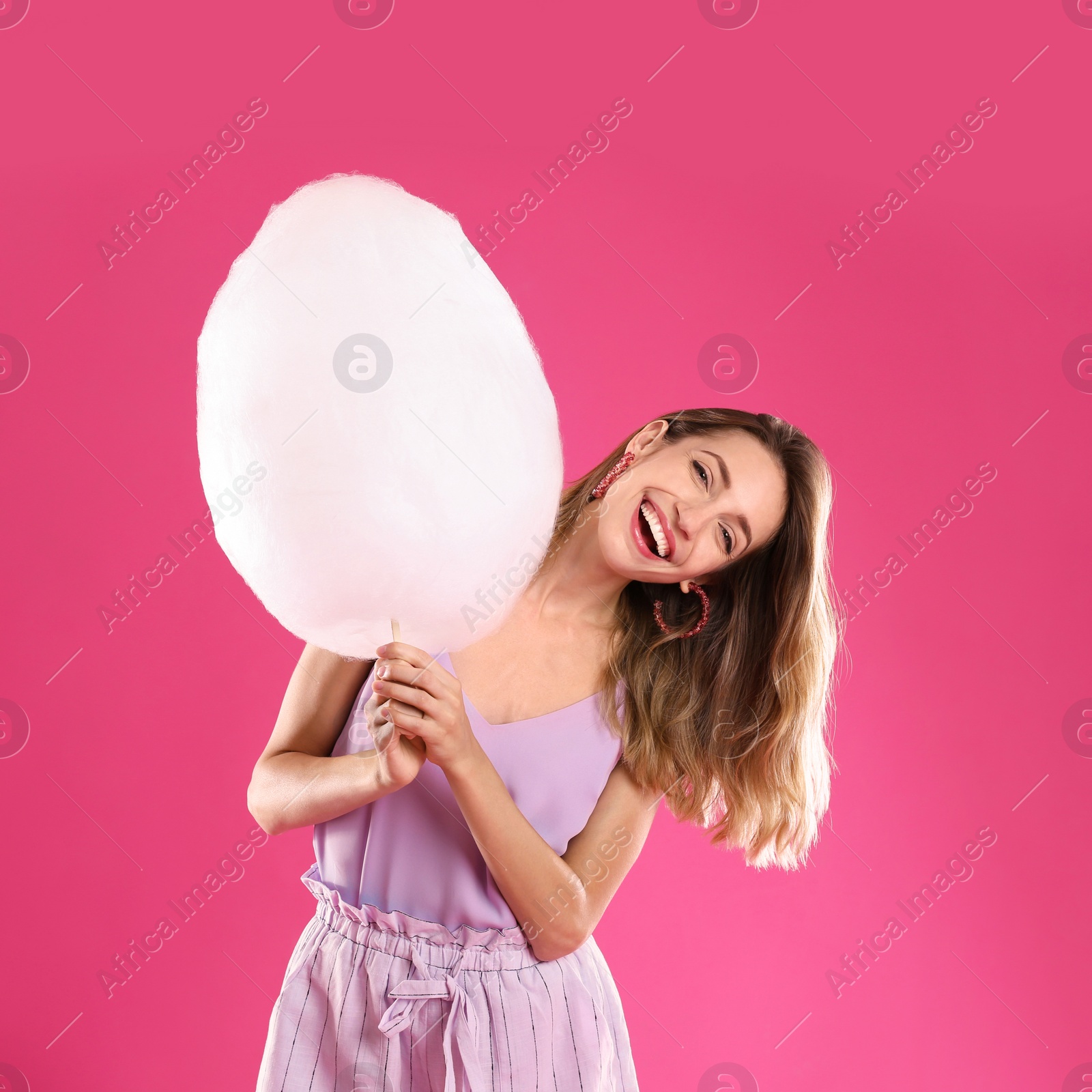 Photo of Happy young woman with cotton candy on pink background