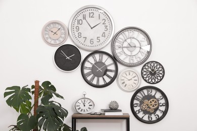 Photo of Console table, beautiful houseplant and collection of different clocks on white wall in room