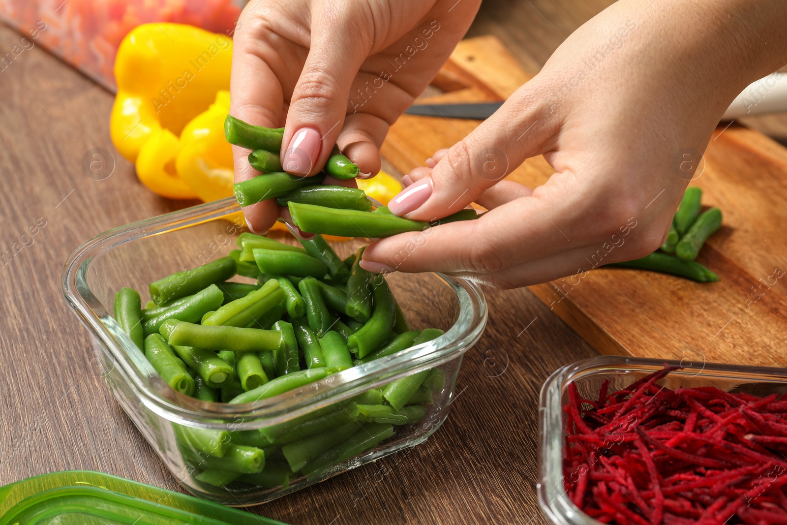 Photo of Woman putting green beans into glass container at wooden table, closeup. Food storage