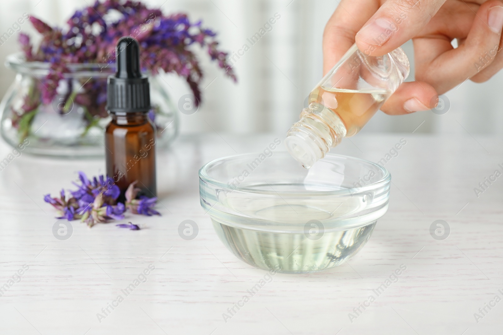 Photo of Woman dripping sage essential oil into bowl on table, closeup