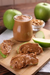 Photo of Slices of fresh green apple with peanut butter on wooden table, closeup