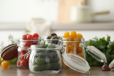 Pickling jars with fresh vegetables on wooden table in kitchen
