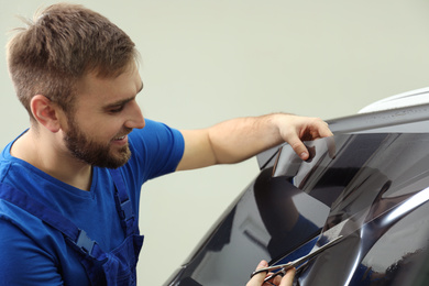 Worker tinting car window with foil in workshop