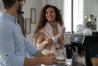Colleagues with hot drinks talking near modern coffee machine in office