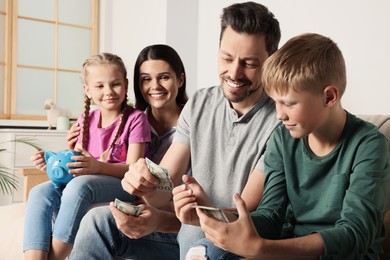Photo of Happy family with money and piggy bank at home