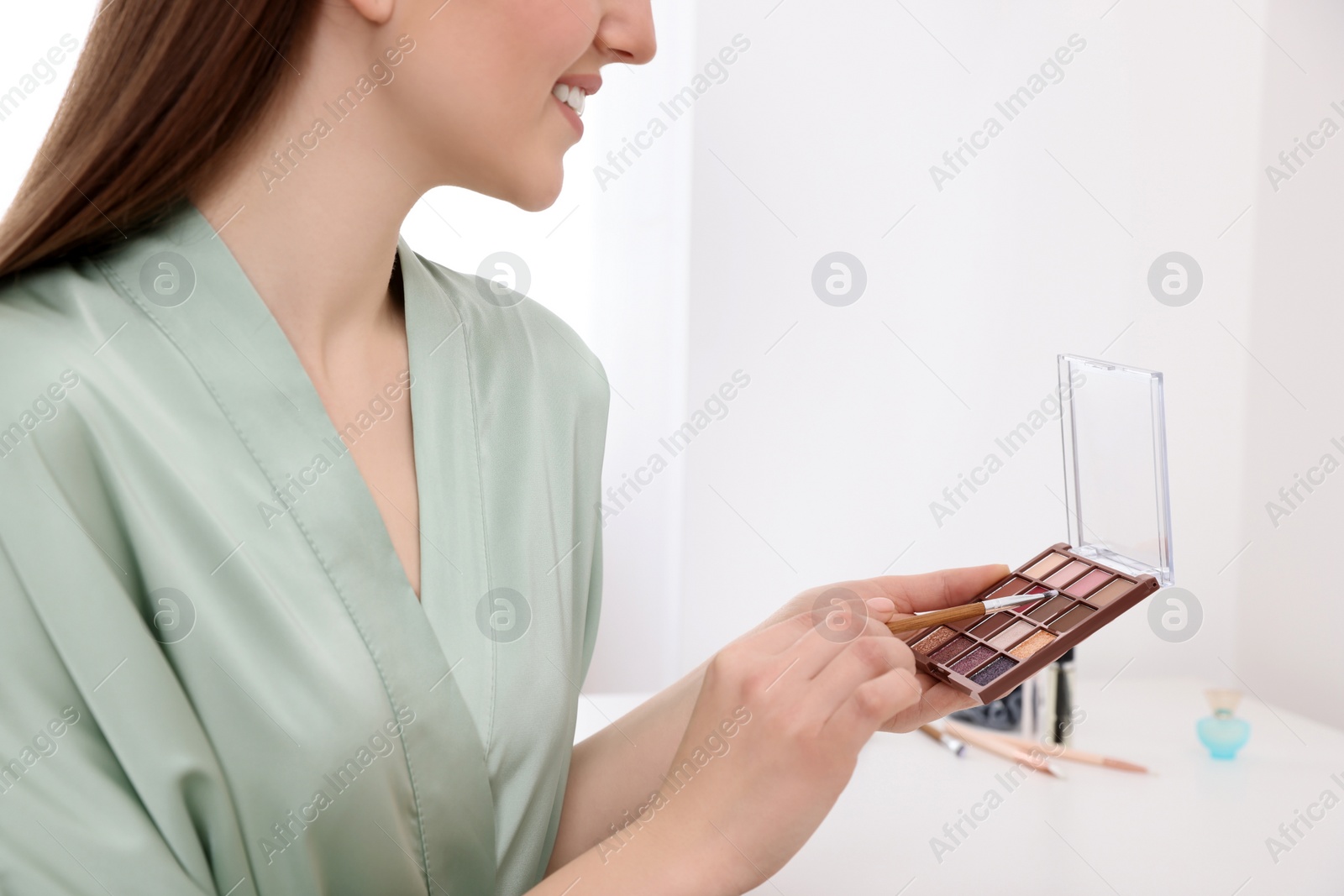 Photo of Woman with eyeshadow palette and brush at dressing table indoors, closeup