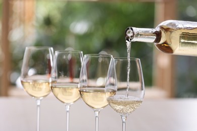 Photo of Pouring white wine from bottle into glass on blurred background