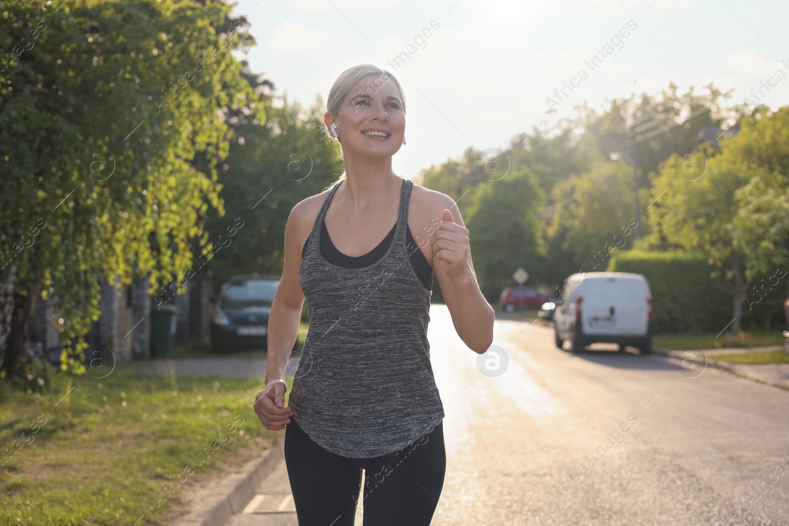 Photo of Woman with wireless earphones jogging around neighborhood in morning