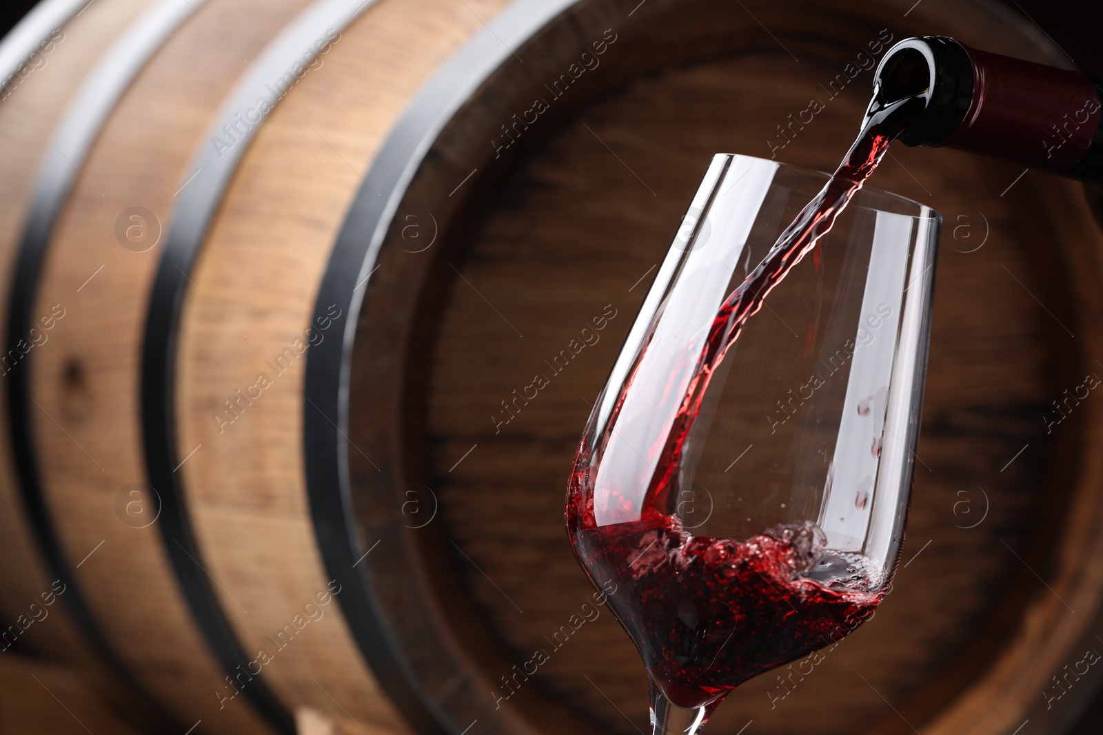 Photo of Pouring delicious wine into glass against wooden barrel, closeup
