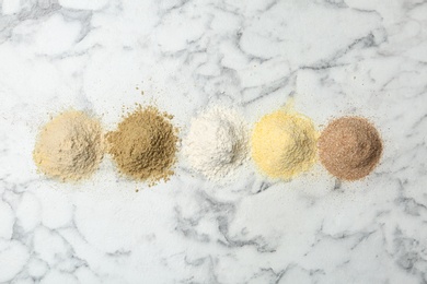 Photo of Piles of different flour types on marble table, top view