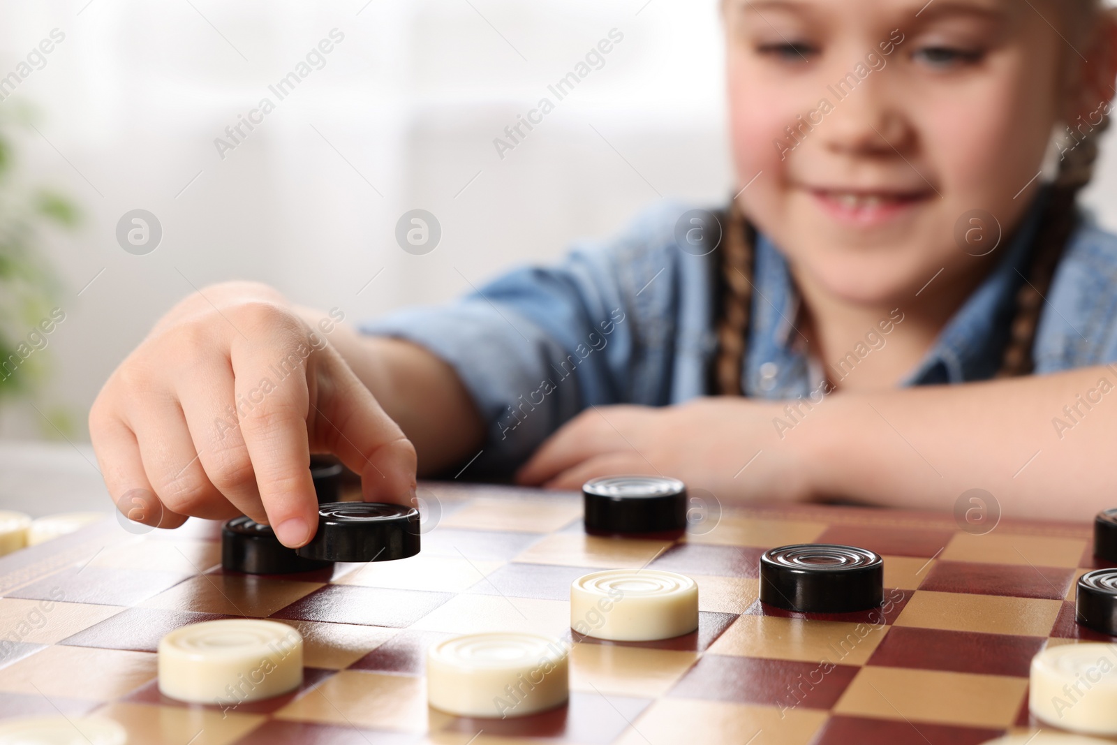 Photo of Playing checkers. Little girl thinking about next move at table in room, closeup