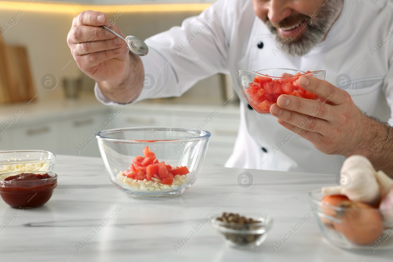 Photo of Professional chef making delicious tomato sauce at white marble table indoors, closeup