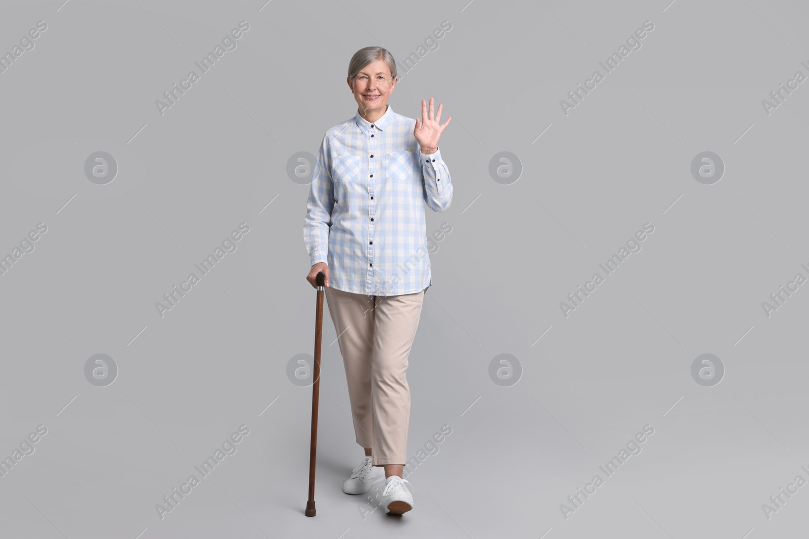 Photo of Senior woman with walking cane waving on gray background