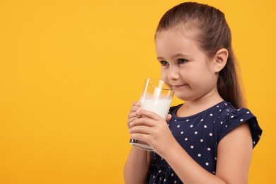 Photo of Cute girl with glass of fresh milk on orange background, space for text