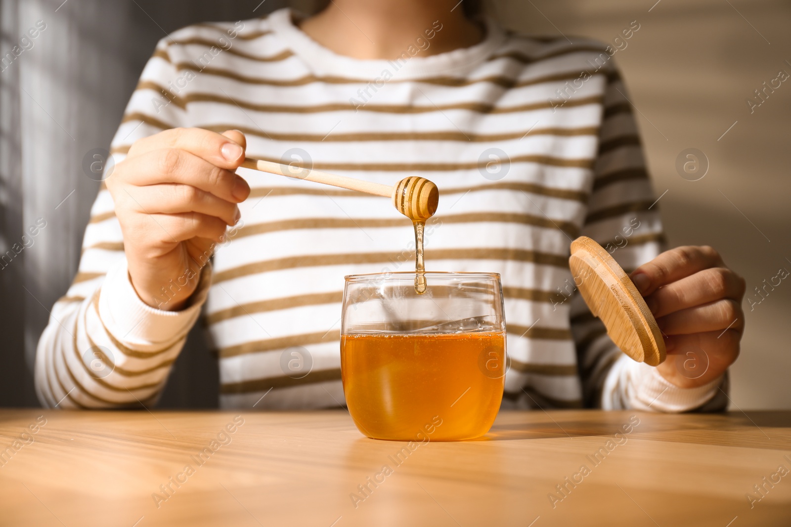 Photo of Woman with honey and dipper at wooden table, closeup