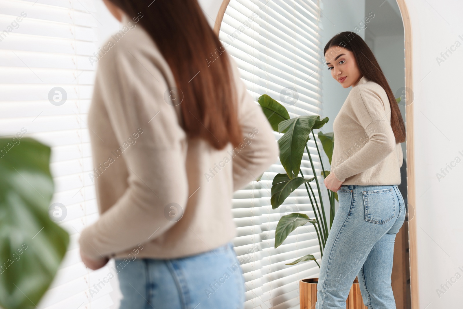 Photo of Young woman in stylish jeans near mirror indoors