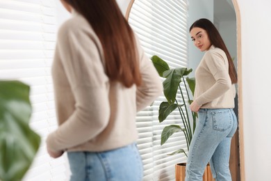 Young woman in stylish jeans near mirror indoors