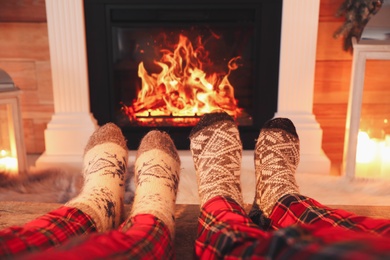 Photo of Couple in warm socks resting near fireplace at home, closeup