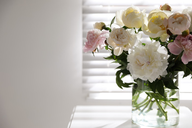 Photo of Beautiful peonies in vase on table near window indoors. Space for text