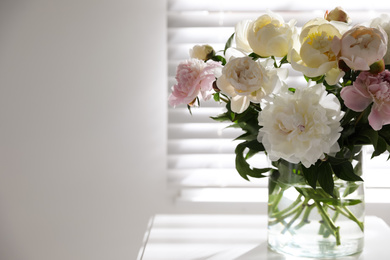 Beautiful peonies in vase on table near window indoors. Space for text