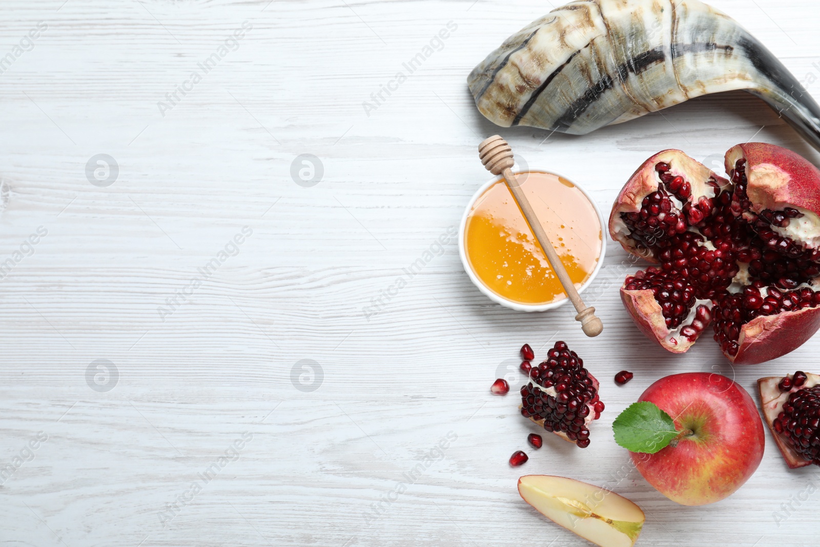 Photo of Honey, pomegranate, apples and shofar on white wooden table, flat lay with space for text. Rosh Hashana holiday