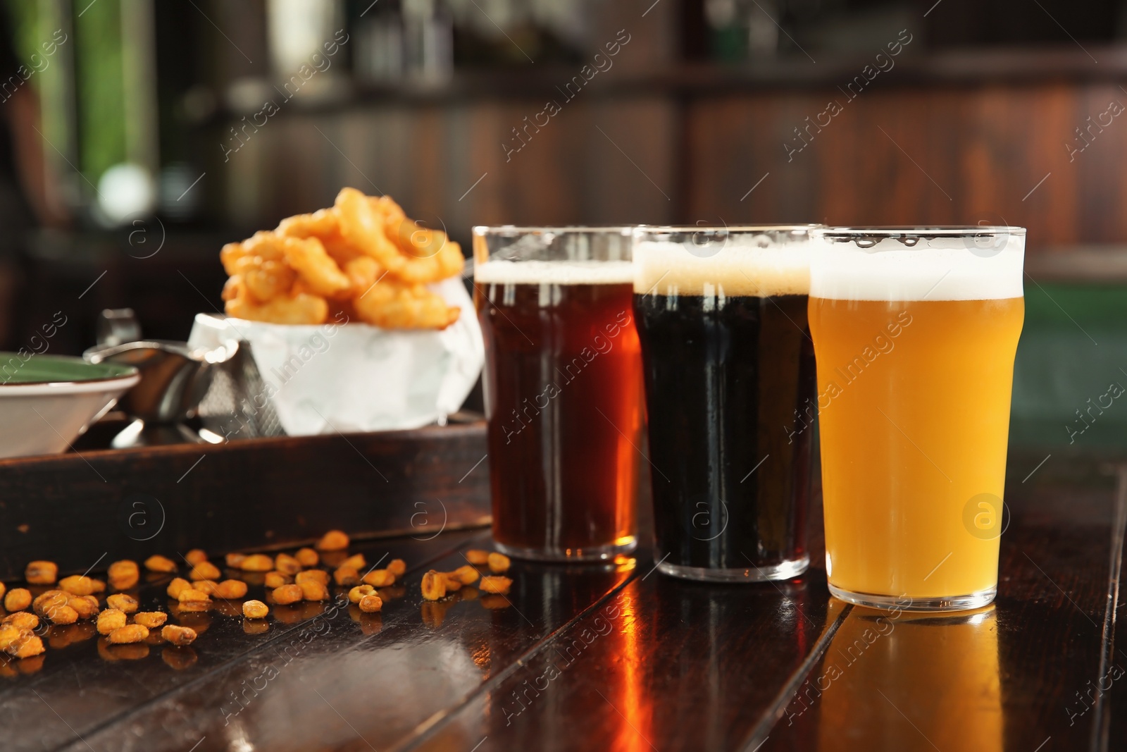 Photo of Glasses of tasty beer and snacks on wooden table in bar