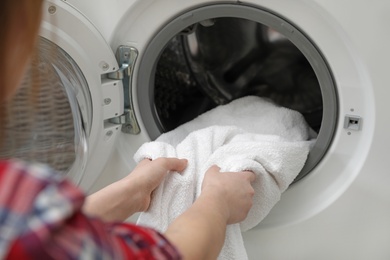 Photo of Woman taking clean towel from washing machine in laundry room, closeup