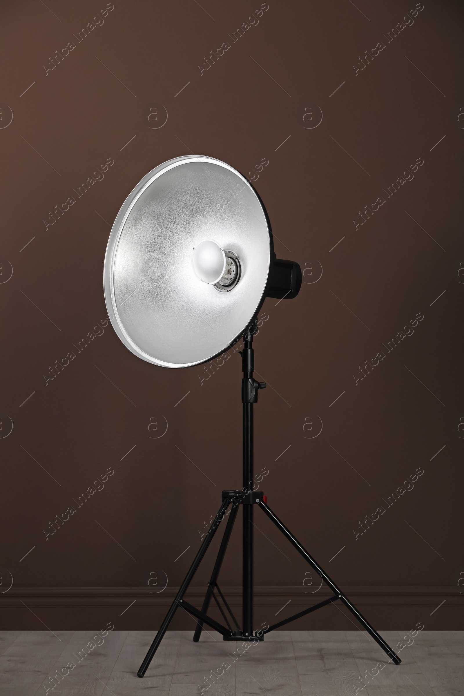 Photo of Professional beauty dish reflector on tripod near brown wall in room. Photography equipment