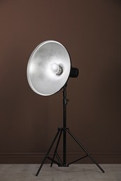 Photo of Professional beauty dish reflector on tripod near brown wall in room. Photography equipment