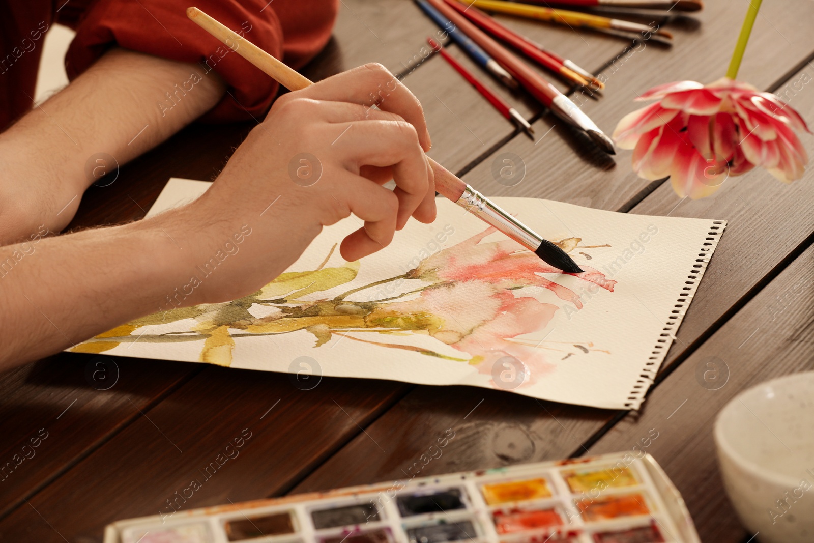 Photo of Woman painting flowers with watercolor at wooden table, closeup. Creative artwork