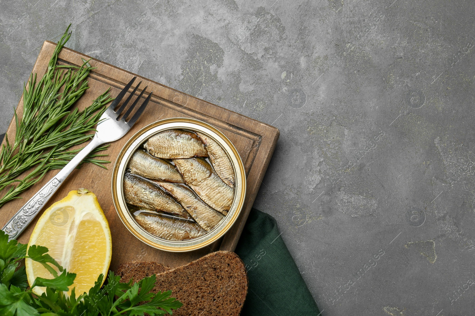 Photo of Tin can with tasty sprats served on grey textured table, flat lay. Space for text