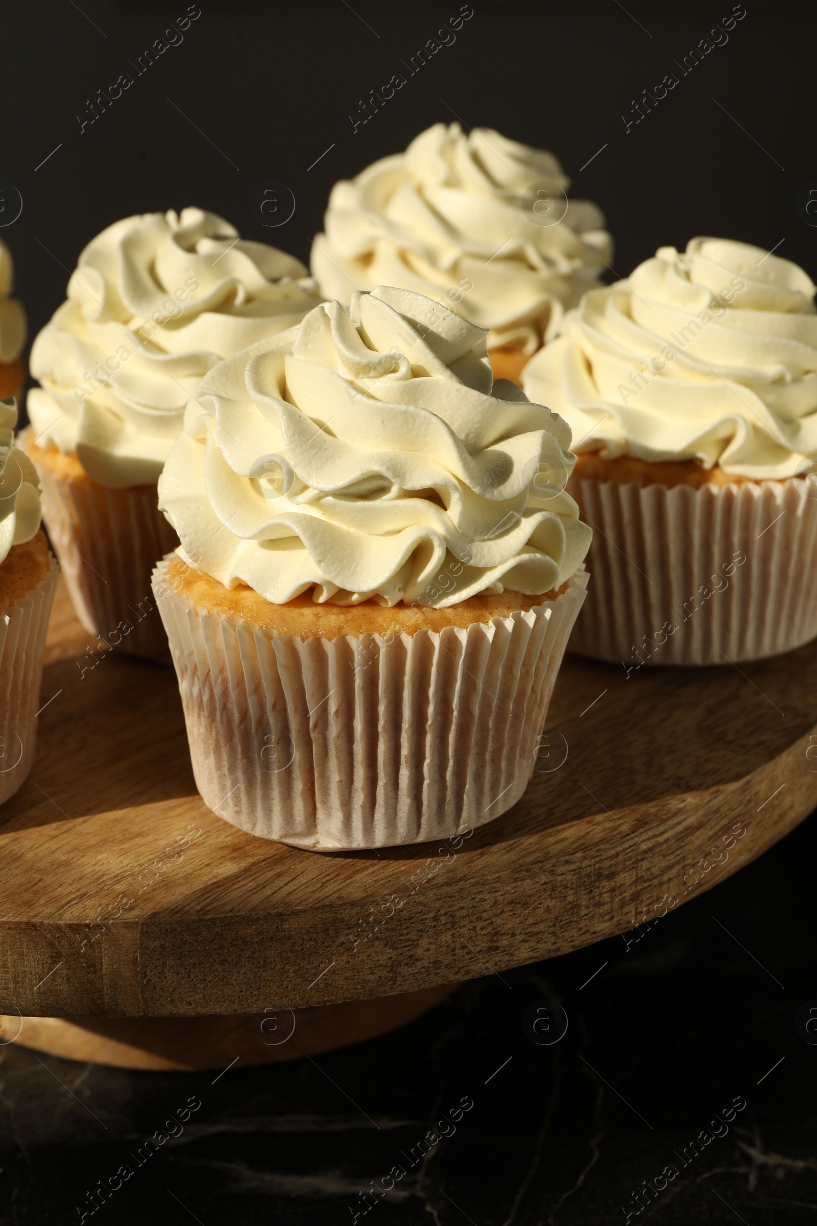 Photo of Tasty cupcakes with vanilla cream on black table, closeup