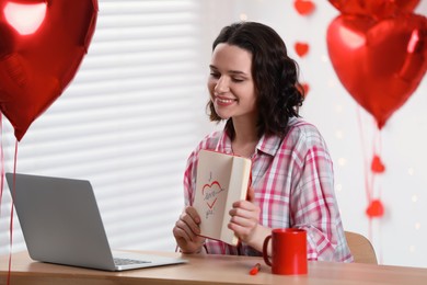 Photo of Valentine's day celebration in long distance relationship. Woman having video chat with her boyfriend via laptop indoors