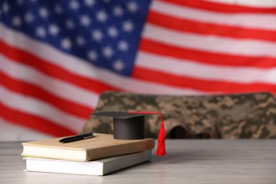 Photo of Notebooks, mortarboard and pen on wooden table against flag of USA, space for text. Military education