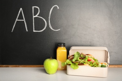 Photo of Healthy food for school child in lunch box on table near blackboard with chalk written letters