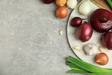 Fresh onion bulbs, leek and garlic on grey table, flat lay. Space for text