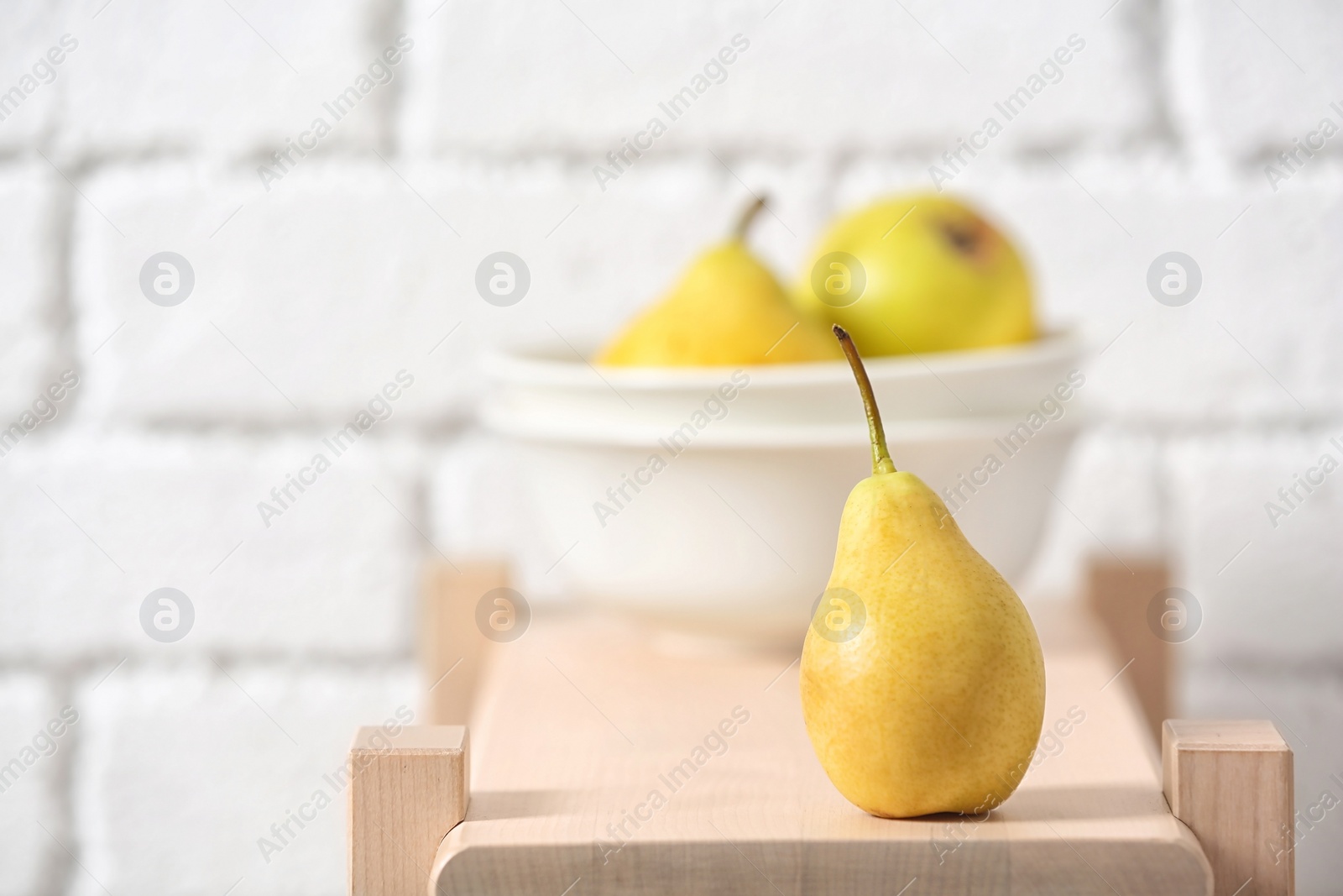 Photo of Ripe pear on wooden shelf against blurred background. Space for text