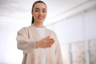 Photo of Happy young woman offering handshake indoors, focus on hand. Space for text