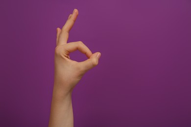 Photo of Woman showing okay gesture on purple background, closeup. Space for text