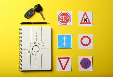 Flat lay composition with workbook for driving lessons and road signs on yellow background. Passing license exam